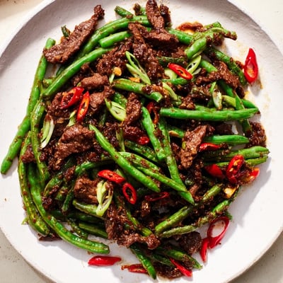 Close-up of Spicy Szechuan Green Beans with Beef with steam rising and sesame seeds scattered over the stir-fry.