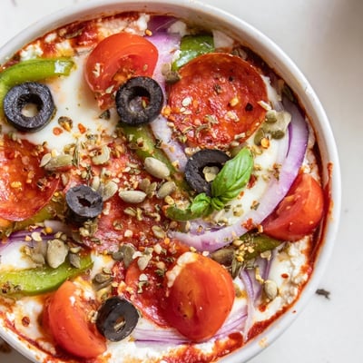 Baked cottage cheese pizza bowl overflowing with melted cheese and colorful vegetables